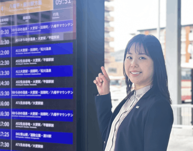 バスターミナルの時刻表の電光掲示板を指さす